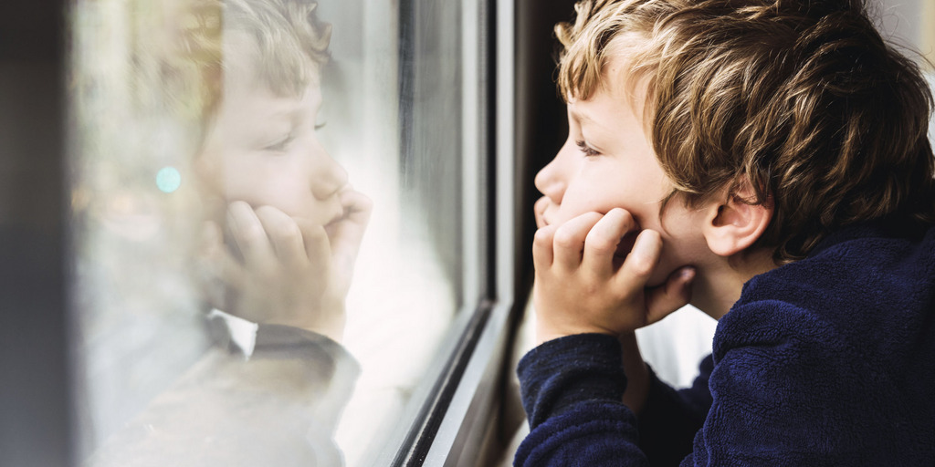 Porträt eines Jungen, der gelangweilt aus dem Fenster seines Zimmers schaut.